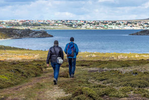 Two people walk towards a view of Stanley on the Falkland Islands.