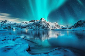 norway lofoten islands green and blue aurora colours over mountain reflecting in water